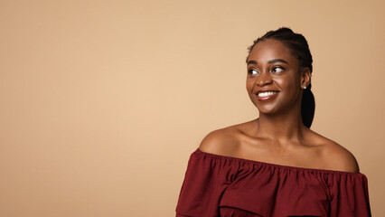 Pretty afro-american millennial woman looking at copy space for text and smiling, beige studio background, panorama. Interested cheerful attractive black lady watching nice advertisement