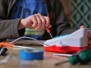 Child's Hands Using a Toy Screwdriver to Repair a Toy Cash Register - Young Person Learning STEM Skills by Fixing Electronics at a Table