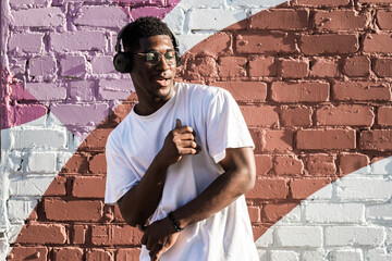 Man dancing with headphones against painted brick wall. Music enjoyment, personal freedom, and self expression through urban street culture © satura_