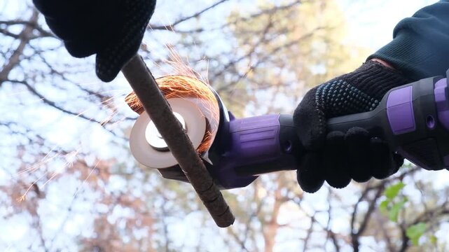 Close up of a mechanic hands in gloves using a cordless cut off saw to cut a thin metal pipe with flying sparks. A battery powered electric tool for construction, repair, and metal cutting work.