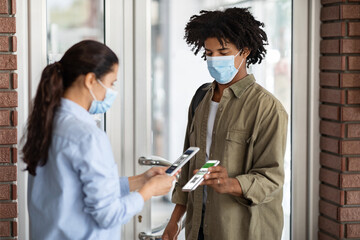 Female Worker With Smartphone Scanning Digital Covid-19 Vaccination Certificate Of Customer On Entrance To Cafe, Young African American Man Demonstrating Health Passport On Mobile Phone Screen