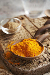 Turmeric root powder on a wooden spoon with ground black pepper in the background