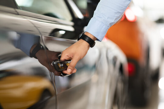 Unrecognizable man open car door, closeup of male hand with watch unlocking black auto door, making test drive at newest automobile showroom. Vehicle, transportation, car salon concept