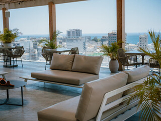 Fototapeta premium Relaxation area on terrace with sofas, plants and urban ocean view from rooftop