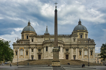 Naklejka premium View of the baroque facade of Santa Maria Maggiore papal basilica with ancient Egyptian obelisk on Piazza dell'Esquilino under dramatic cloudy summer sky