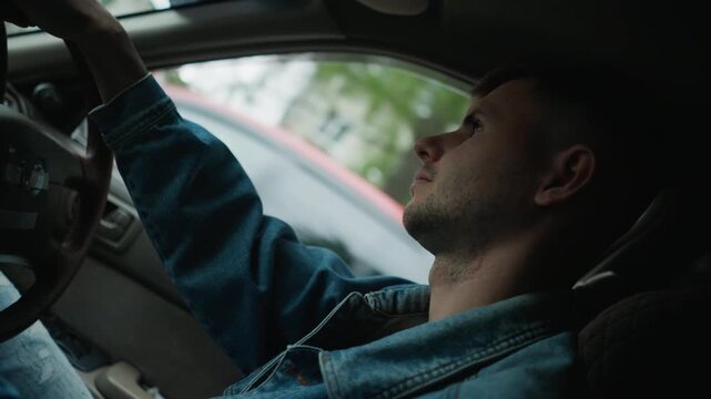 white man in denim behind wheel, leaning back and staring out window, glancing at rearview mirror and taking a slow breath urban street outside, soft cinematic grain, moody afternoon light, solitary