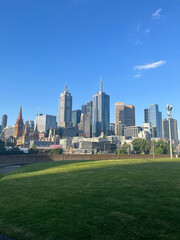 Obraz premium Melbourne skyline with skyscrapers and green park lawn under a clear blue sky