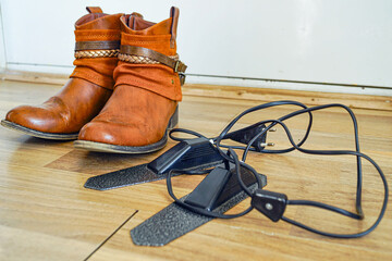 Brown eco-leather ankle boots with decorative straps placed next to electric shoe dryer on floor. Symbolizes footwear care routine, moisture removal, odor prevention, and prolonged shoe lifespan.