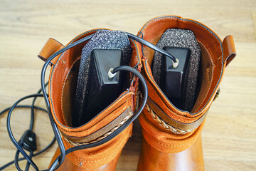 Overhead view of electric dryer inside women's boots. Illustrates thermal drying mechanism, foot health, moisture control, functional domestic hygiene, and wellness focused footwear management.