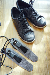 Black sneakers and electric dryer pads. Symbolizes climate humidity issues, microbial risk awareness, urban walking culture, foot health prevention, anti odor technology, and minimalist hygiene tools.