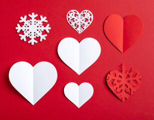 Paper cutouts of hearts and snowflakes arranged on a vibrant red background