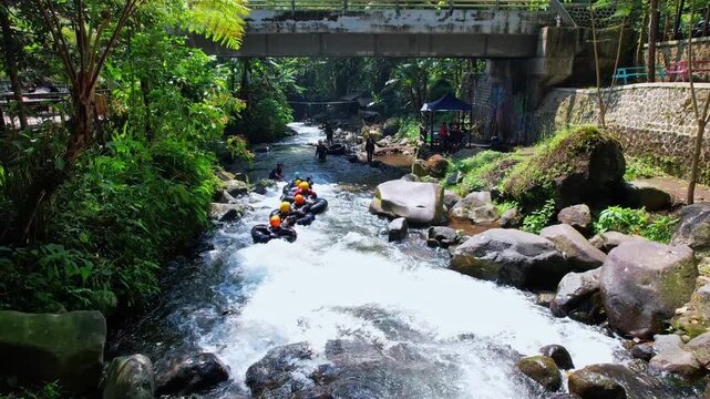 Aerial drone footage of a small natural river, with forest around, at sunrise, in Cikadongdong river, Majalengka regency, Java island, Indonesia, with a bridge behind and people going down on buoy