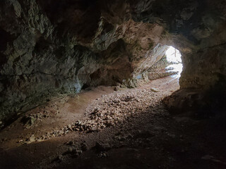 Moody interior view of the Szeleta Cave with a rocky path leading toward the bright cave exit,...