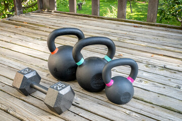 iron dumbbell and  kettlebells on a wooden backyard deck, home gym concept