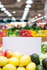 Fresh lemons and avocados are displayed prominently in a vibrant market setting with colorful fruits and vegetables in the background, featuring ample copy space for design purposes