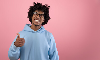 Sincere black teen guy showing thumb up gesture, expressing approval on pink studio background, banner with copy space. Confident Afro teenager confirming or agreeing to something