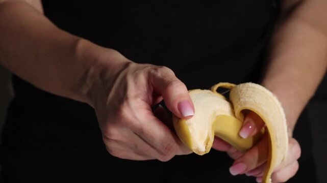 Woman peels a banana in a close-up shot showing hands and fruit details during a casual moment. Hands hands hold a banana and peels it with both hands