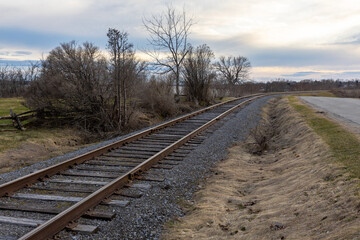 Fototapeta premium Railway tracks running through rural landscape at dusk in early spring