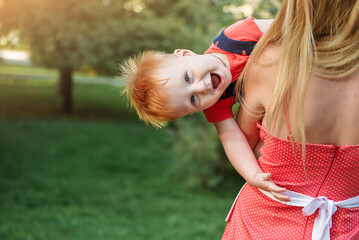 Mom and son are playing cheerfully together in the park in the summer. Mother is holding the baby boy in her arms.