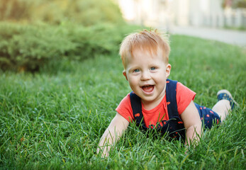The boy is lying on the grass and laughing. Baby is playing cheerfully in the park in the summer.