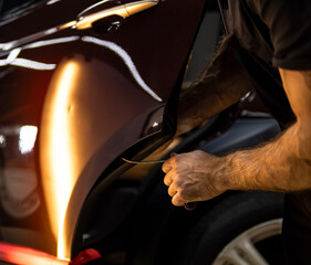 Process of paintless dent repair on car body. The mechanic at the auto shop with tools to repair dents in car body. Body repair. A specialist repairs a dent on the car body without painting. PDR. 