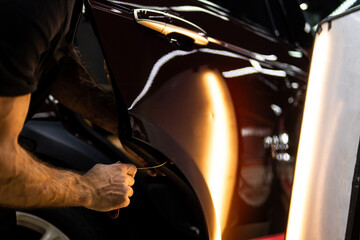 Process of paintless dent repair on car body. The mechanic at the auto shop with tools to repair dents in car body. Body repair. A specialist repairs a dent on the car body without painting. PDR. 