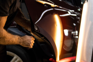 Process of paintless dent repair on car body. The mechanic at the auto shop with tools to repair dents in car body. Body repair. A specialist repairs a dent on the car body without painting. PDR. 