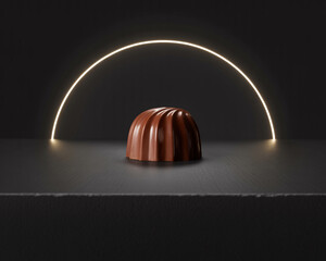Single milk chocolate praline with fluted sides on a dark surface under a glowing arc light