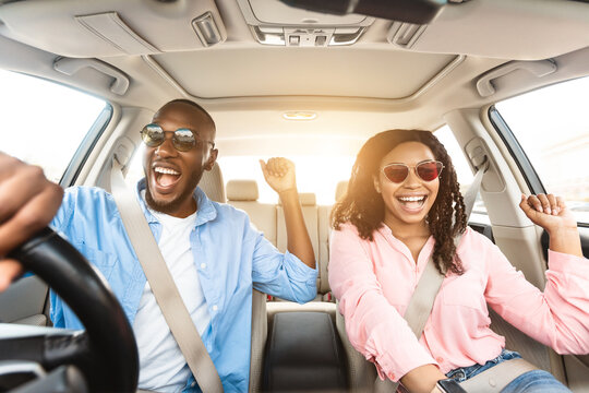 Summer Holidays And Roadtrip Concept. Front view portrait of excited black couple in sunglasses driving car, dancing to music and singing favorite song, going on vacation for rest and relax, sun flare