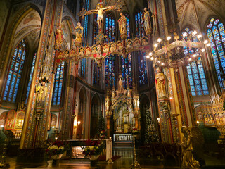 The ornate interior of De Krijtberg church in Amsterdam, featuring detailed gothic architecture, stained-glass windows, and a large golden crucifix hanging above the altar with christmas trees