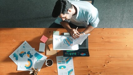 Top aerial view of manager working on laptop while looking at data analysis. Leader compare financial statistic graph while making decision at meeting table with document scatter around. Convocation.