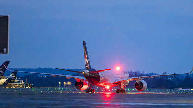 Ein Airbus A350 der Lufthansa rollt bei D&auml;mmerung &uuml;ber das beleuchtete Rollfeld. Das Langstreckenflugzeug ist mit aktiven Positionslichtern ausgestattet und bereitet sich auf den Abflug vor. 