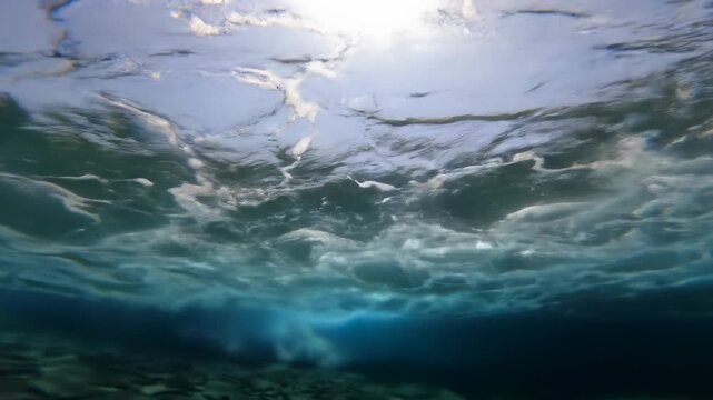 Extreme low-angle POV video from beneath ocean, massive, powerful wave curls and breaks overhead, golden hour sunlight pierces water, caustics and flares. Concept of raw ocean power