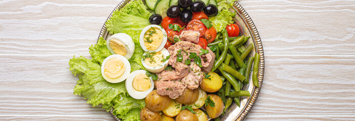 Nicoise salad with tuna, eggs, potatoes, green beans, and olives on a white table