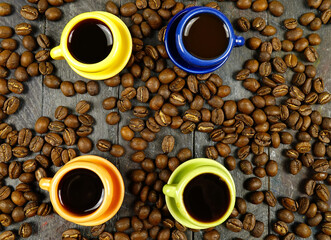 Small colorful cups with hot black coffe among scattered coffee beans are on a black wooden board, top view
