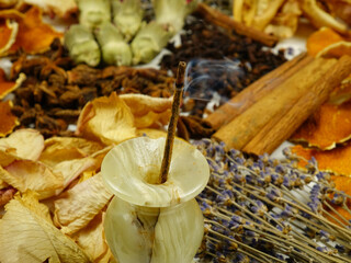 Dried herbs, flowers, spice, orange peel and burning incense stick in an onyx incense holder, top view,  background. Ingredients for air freshening and relaxation.