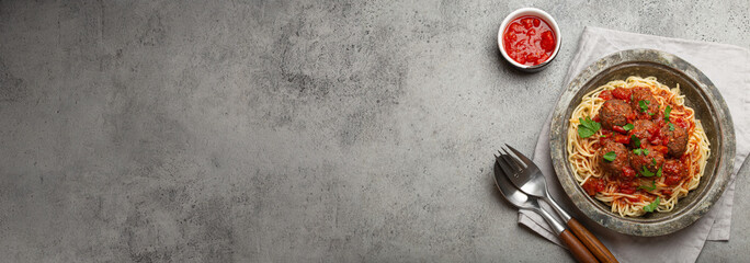Spaghetti and meatballs with tomato sauce served on rustic plate with cutlery top view copy space