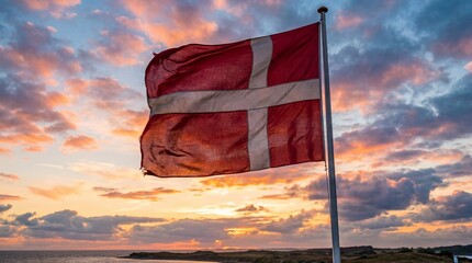 Danish flag (dannebrog) waving against a vibrant sunset sky over a coastal landscape
