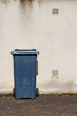 Naklejka premium Large grey wheel bin in front of a wall. Garbage container for sorting garbage in a french city. Waste container placed in front of a beige wall.