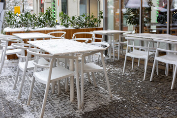 Empty outdoor cafe terrace with white plastic tables and chairs covered with snow in winter.