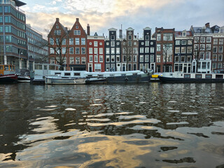 Amsterdam canal houses with snowy roofs and houseboats reflect in the water, capturing a chilly winter day in the historic city