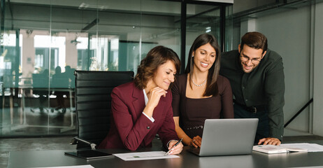Mature Latin business woman and European young team working using laptop computer in office. Diverse colleagues coworkers group of professional business people discussing project. Banner, copy space