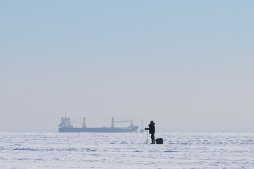 Traditional ice fishing activity on big water in cold winter season. Man fisher preparing hole in...