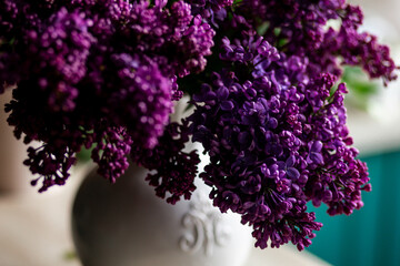 Beautiful bouquet of purple lilac flowers in a white vase. Floral decor for home decor