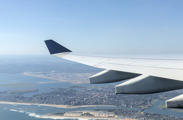 airplane wing flying over the rockaways after taking off from new york city airport heading east over atlantic ocean long island beach waves sand houses neighborhood arverne edgemere apartments