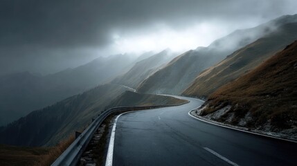 Scenic winding road through dramatic mountain landscape under cloudy sky with shadows and mist, perfect for travel and adventure themes in photography