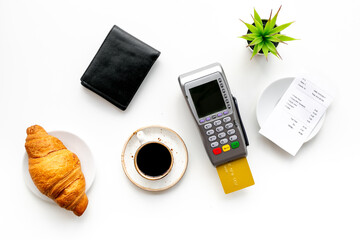 Paying the bill by pos terminal in cafe or restaurant. Cup of black coffee and croissant, payment wireless machine and bill on white background, top view