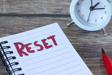 Reset, handwritten word in notebook with alarm clock on wooden desk. Close-up. Time management, new...