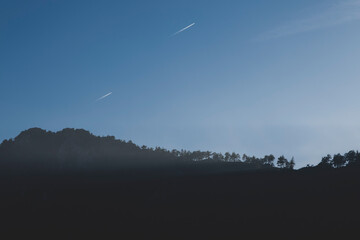 Blue Sky with Mountain and Tree Silhouette. Minimal Mountain Landscape Under Clear Blue Sky. Tree and Mountain Silhouette Against Blue Background. Scenic Mountain Ridge with Forest Silhouette.
