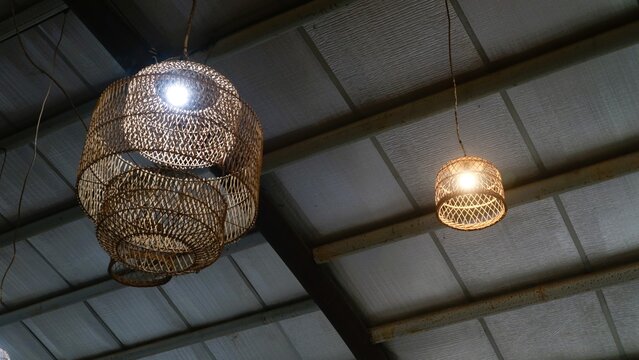 Two woven rattan pendant lamps hanging from a metal ceiling with exposed beams in a warehouse or industrial setting.